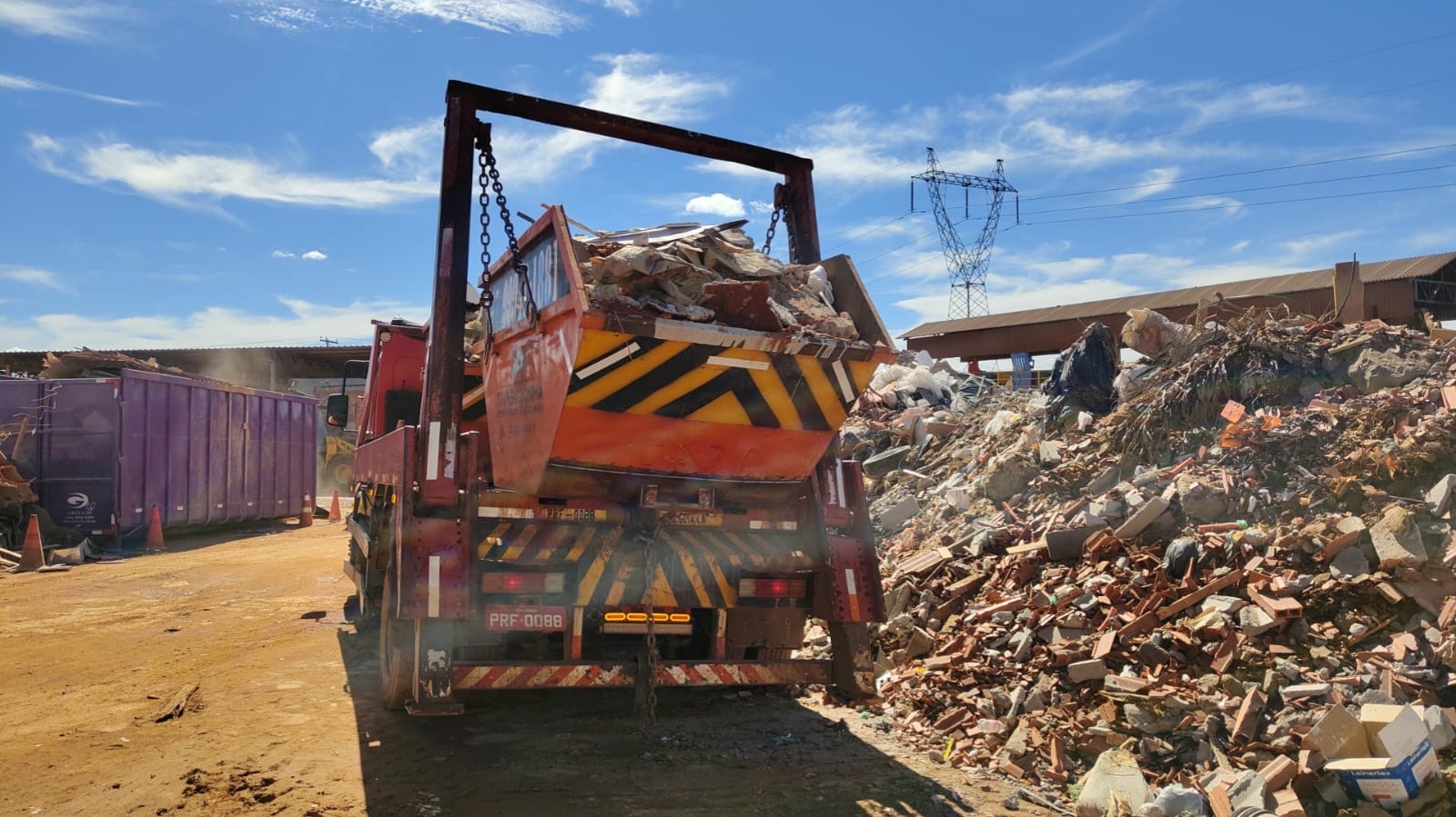 Caçamba carregada de entulho de reforma sendo erguida pelo caminhão
